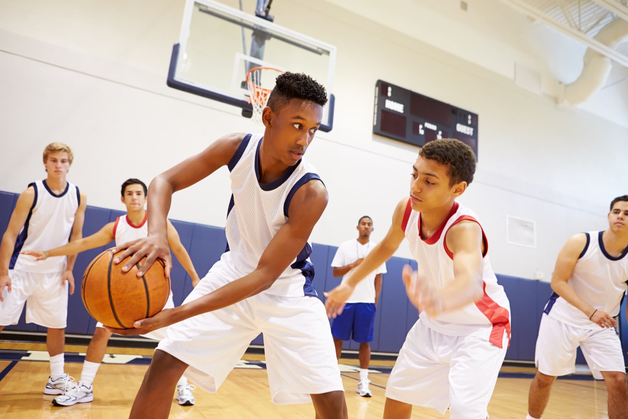 High school players run a drill at basketball practice while a coach watches